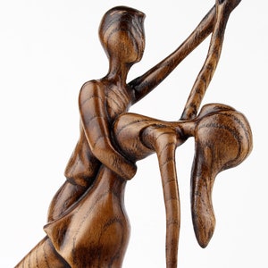 May include: A wooden sculpture of a couple dancing. The man is holding the woman in his arms, and they are both smiling. The sculpture is made of dark wood and has a rustic finish.
