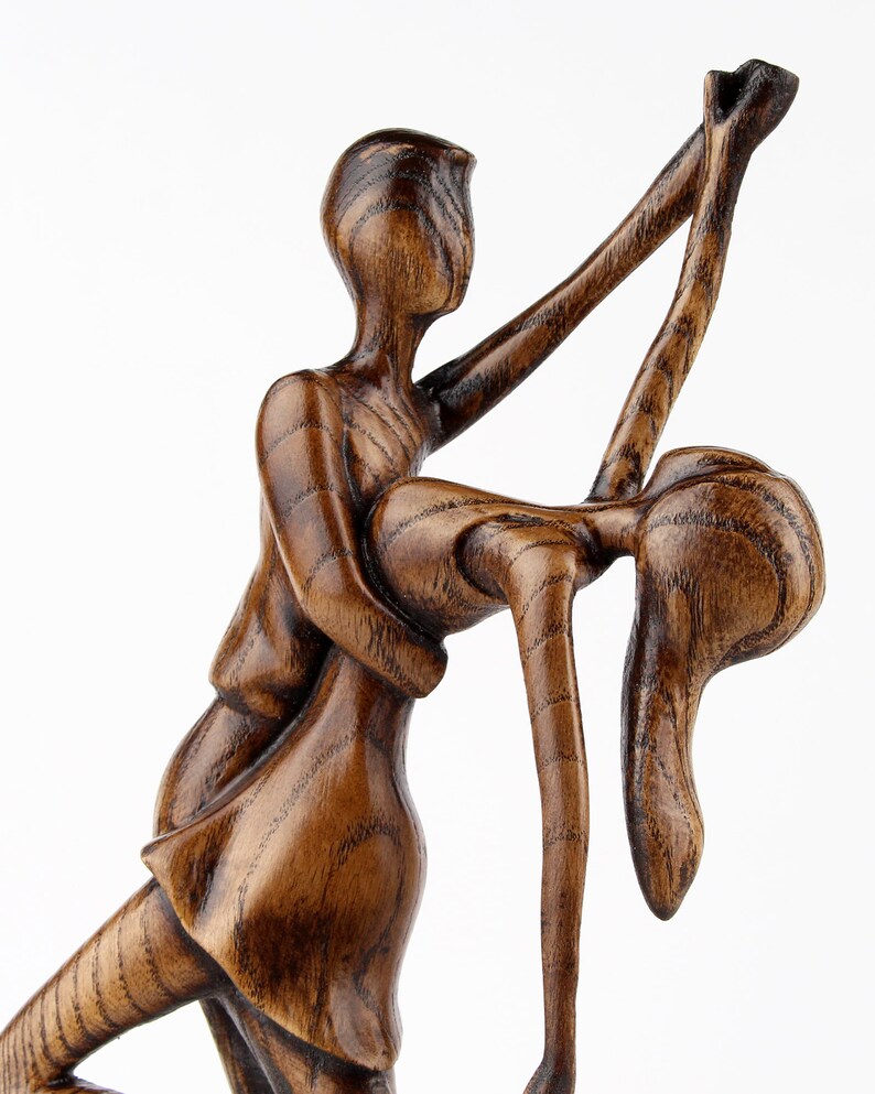 May include: A wooden sculpture of a couple dancing. The man is holding the woman in his arms, and they are both smiling. The sculpture is made of dark wood and has a rustic finish.