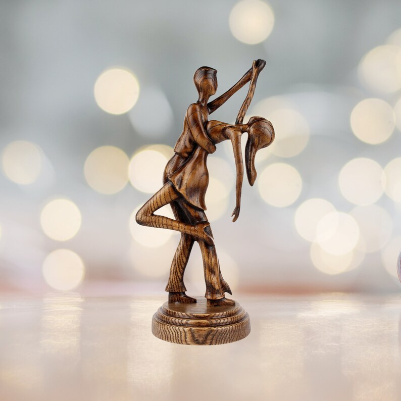 May include: A wooden sculpture of a couple dancing. The man is holding the woman in his arms, and they are both smiling. The sculpture is painted in a dark brown color and has a rustic finish.