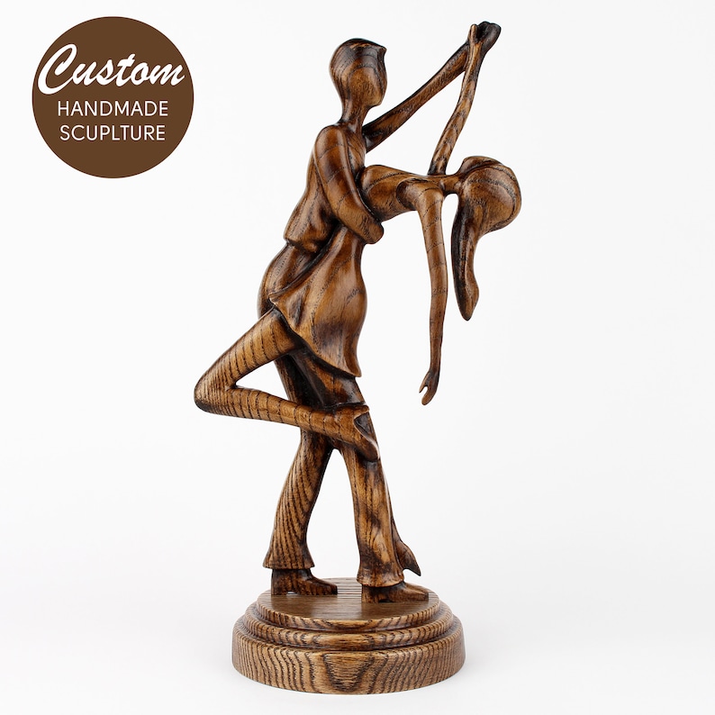 May include: A wooden sculpture of a couple dancing. The man is holding the woman in his arms, and she is leaning back. The sculpture is made of dark wood and has a natural finish.
