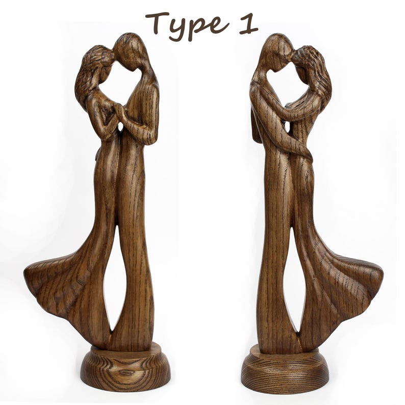May include: A wooden sculpture of a couple embracing, with the woman's dress flowing behind her. The sculpture is stained a dark brown colour and stands on a round base.