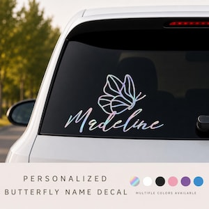 May include: A holographic butterfly decal applied to a car rear window, featuring the name Madeline in a cursive script font. The design consists of thin, iridescent lines forming the butterfly shape above the personalised name text.
