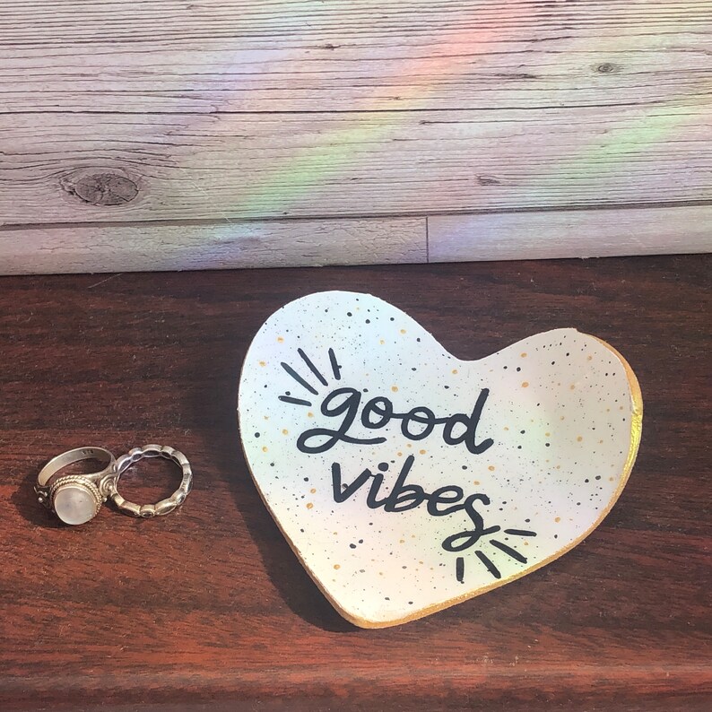 May include: White heart-shaped ceramic dish with gold speckles and black lettering that reads "good vibes".