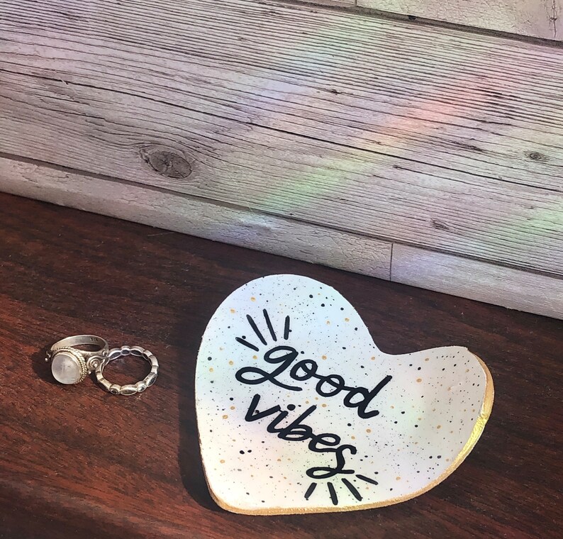 May include: White ceramic heart-shaped dish with gold speckles and black lettering that reads "good vibes".
