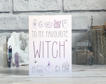 May include: A white card with purple text that reads "To my favorite witch". The card is decorated with illustrations of various witchy items, including a crescent moon, a crystal, a book, a cauldron, and candles.