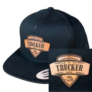 Könnte beinhalten: Schwarze Trucker-Kappe mit einem braunen Leder-Patch, auf dem "TRUCKER" mit einer Krone und Sternen steht.