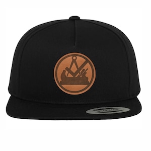 May include: Black and brown baseball cap with a leather patch featuring a compass, square, and plane. The patch is in the center of the cap.