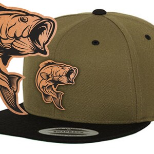 Könnte beinhalten: Eine grüne und schwarze Baseballkappe mit einem schwarzen Fisch-Motiv auf der Vorderseite. Der Fisch springt mit offenem Maul.