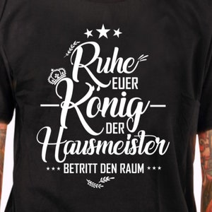 Peut inclure: T-shirt noir avec un texte blanc qui dit "Ruhe Euer König Der Hausmeister Betritt Den Raum" avec trois étoiles au-dessus du texte et une couronne et deux brins de feuilles en dessous du texte.