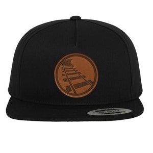 Può includere: Cappellino da baseball nero e marrone con una toppa in pelle che presenta un design di binari del treno.