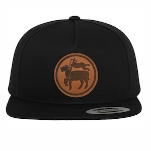 Op de afbeelding: Zwarte en bruine baseballpet met een leren patch met een gestileerd beeld van een lam dat op een voetstuk staat met een vlag.