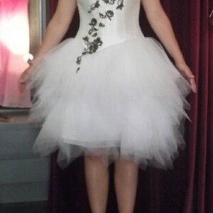 Könnte beinhalten: Ein weißer Tüllrock mit schwarzem Blumendesign auf dem Oberteil. Der Rock ist geschichtet und hat einen Rüschen-Saum. Das Model trägt weiße Absätze.