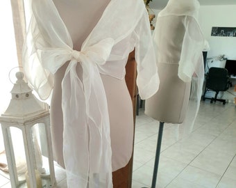 May include: A white sheer shawl with a bow tie detail. The shawl is draped over a white mannequin and is displayed against a mirror.