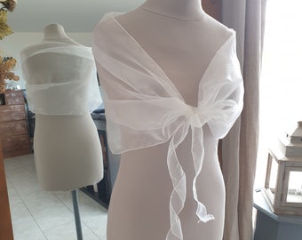 May include: White sheer shawl with a bow tie detail. The shawl is made of a lightweight fabric and is perfect for adding a touch of elegance to any outfit.