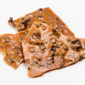 May include: Close-up of three pieces of pecan brittle, a sweet and crunchy treat made with pecans, sugar, and butter. The brittle is a light brown colour and has a glossy finish.