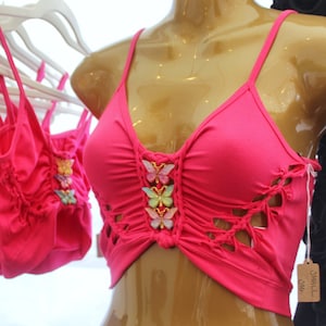 May include: Pink crop top with butterfly embellishments and a cutout design. The top is on a mannequin and has a tag that says "Small One".