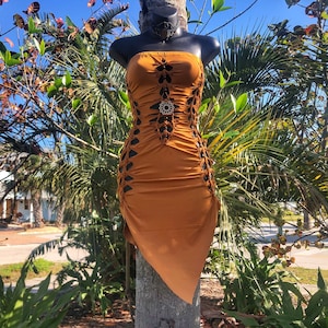 Op de afbeelding: Een roestkleurige strapless jurk met uitsnijdingen en een geometrisch ontwerp. De jurk is gemaakt van een rekbaar materiaal en heeft een aansluitende pasvorm.