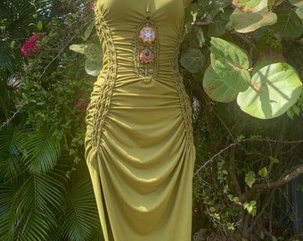 May include: A long, olive green maxi dress with a fitted bodice and a flowing skirt. The dress has a unique design with a braided detail and decorative buttons on the front.