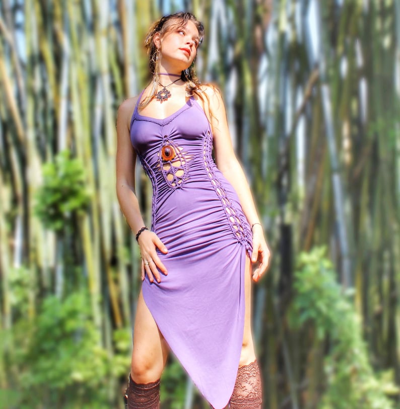 Puede incluir: Un vestido lavanda con cuello halter y detalles de macram&eacute; en el corpi&ntilde;o y los laterales. El vestido presenta una falda fruncida y un dobladillo asim&eacute;trico. Una gran piedra ovalada marr&oacute;n est&aacute; centrada en el corpi&ntilde;o. El vestido se lleva con calcetines altos hasta la rodilla con encaje marr&oacute;n.