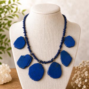 May include: A striking necklace featuring large, irregular, deep blue stone pendants. The pendants are suspended from a beaded navy blue chain. The necklace is displayed on a mannequin, showcasing its unique design and color.
