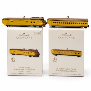 May include: Two Hallmark Keepsake ornaments featuring Lionel Union Pacific train cars. One is a yellow and brown streamliner locomotive, and the other is a matching long coach. Both ornaments are displayed on their respective white product boxes.