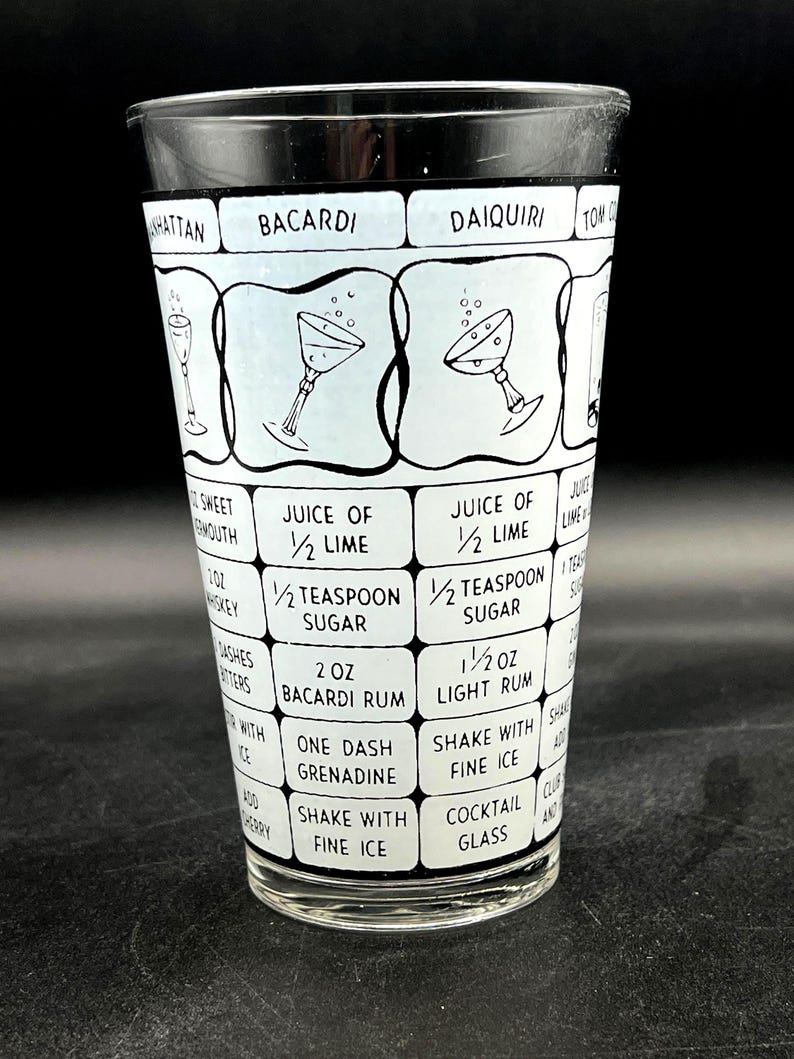 May include: A clear cocktail mixing glass with a black rim and a white and light blue design. The glass features cocktail names and ingredient lists, including "Bacardi" and "Daiquiri". The design includes illustrations of cocktail glasses.