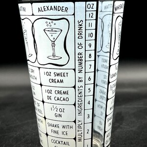 May include: A clear cocktail shaker glass with a black and white design. The glass features cocktail recipes, including the "Alexander" cocktail, and a scale for measuring ingredients. The text includes measurements in ounces.
