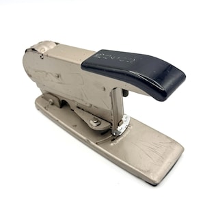 May include: A vintage silver stapler with a black handle. The stapler has visible wear and tear, suggesting it has been used. The word "BOSTITCH" is printed on the black handle. The stapler is on a white background.