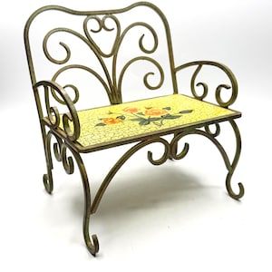 May include: A miniature decorative bench with a yellow mosaic seat featuring orange floral designs. The metal frame is a dark gold color with ornate scrollwork on the back and arms. The bench has curved legs.