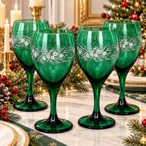 May include: A set of four emerald green wine glasses, each featuring a delicate white etched design of pine branches and pinecones encircling the bowl. The glasses have a smooth, rounded bowl, a slender stem, and a stable circular base.