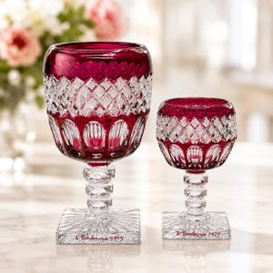 May include: Two ruby red crystal wine glasses with intricate diamond and arched patterns. The glasses have square bases with the text "E. Barbero 1979". The stemware is a classic design, perfect for special occasions.