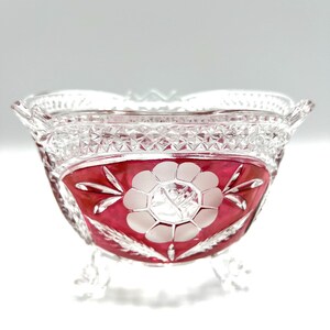 May include: A clear glass bowl with a red and white floral design. The bowl has a scalloped rim and three feet.