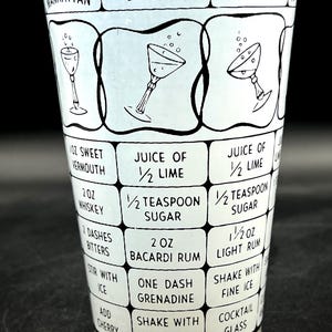 May include: A vintage cocktail shaker with a black and white design. The shaker features recipes for Manhattan, Bacardi, and Daiquiri cocktails, including ingredient measurements in ounces and teaspoons. The glass has a black rim and a clear base.
