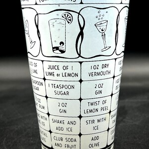 May include: A vintage cocktail shaker with a black and white design. The shaker features recipes for classic cocktails like Tom Collins and Martini, with ingredient measurements and instructions. The glass is clear.