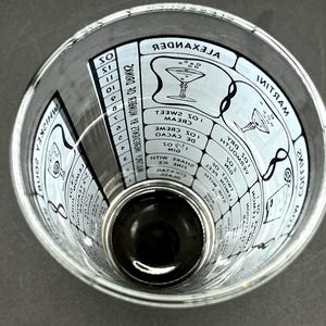May include: A clear cocktail mixing glass with white text and illustrations. The glass features cocktail recipes, including measurements and names like "Alexander" and "Martini". The glass is designed for mixing drinks.