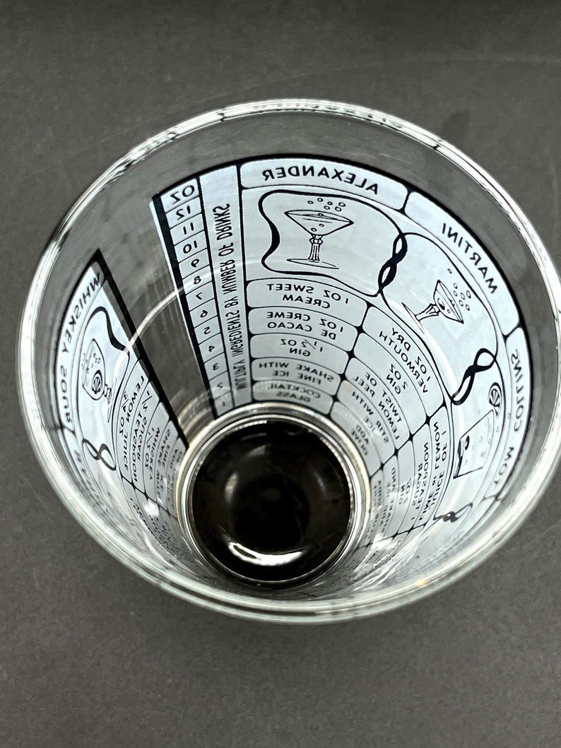 May include: A clear cocktail mixing glass with white text and illustrations. The glass features cocktail recipes, including measurements and names like "Alexander" and "Martini". The glass is designed for mixing drinks.