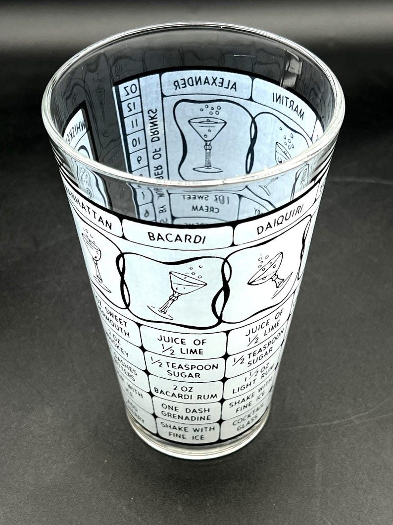 May include: A clear glass cocktail shaker with a black and white design. The shaker features cocktail recipes, including ingredients and instructions for drinks like the Manhattan and Daiquiri. The glass is cylindrical.