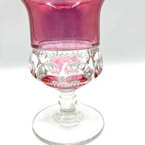 May include: A clear glass goblet with a pink iridescent top and a clear stem and base. The goblet has a decorative pattern of raised dots around the rim and base.