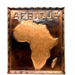 May include: A rectangular copper wall plaque featuring a relief map of the African continent. The word AFRIQUE is embossed at the top. The map displays various country names and borders in a raised metallic finish against a dark background.