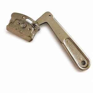 May include: A silver-toned metal tool featuring a hinged, L-shaped handle and a rectangular head with a central screw. The handle includes an embossed inscription that reads Made in USA and a circular hole at the end for hanging or storage purposes.