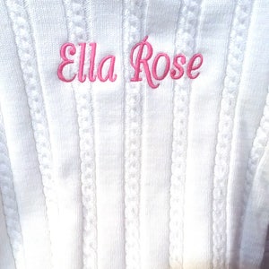 May include: White knitted hooded sweater with a pink embroidered name "Ella Rose"