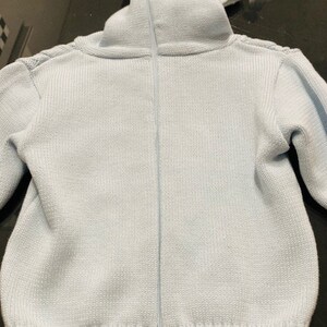 May include: A light blue knitted sweater with a zipper closure. The sweater has a high collar and long sleeves.