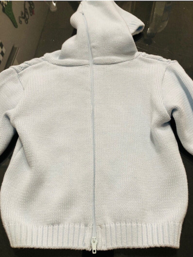 May include: A light blue knitted sweater with a zipper closure. The sweater has a high collar and long sleeves.