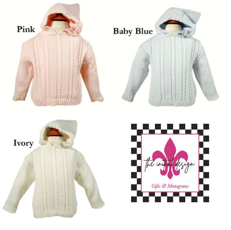 May include: Three hooded cable knit sweaters in pink, baby blue, and ivory. The sweaters have a ruffled trim around the hood. The sweaters are displayed on mannequins. The image includes the text "the initial design Gifts & Monograms".