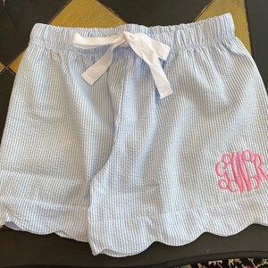 May include: Light blue and white striped shorts with a scalloped hem and a pink monogrammed "CWR" on the right side.