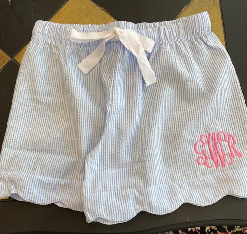 May include: Light blue and white striped shorts with a scalloped hem and a pink monogrammed "CWR" on the right side.