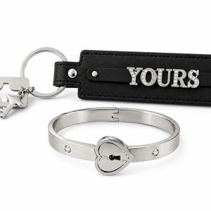 May include: A set of matching accessories, including a black leather keychain with the word "YOURS" in silver, a silver key and keyhole charm, and a silver bracelet with a heart-shaped lock design. The bracelet has small, clear crystals.