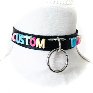 May include: Black leather choker with a silver ring and the word "CUSTOM" spelled out in colorful letters.