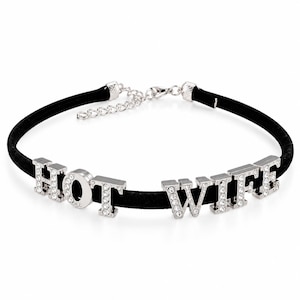 May include: A black velvet choker necklace featuring silver-toned metal letters that spell out the phrase HOT WIFE. Each letter is encrusted with small clear rhinestones. The necklace includes a silver-toned metal chain extender and a lobster claw clasp.