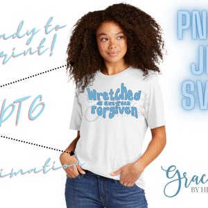 May include: A white t-shirt with the text "Wretched and I am forgiven" in blue lettering. The shirt is being modeled by a person with curly brown hair. The image also includes the text "Ready to print!" and "BTG Sublimation" in blue and pink lettering.